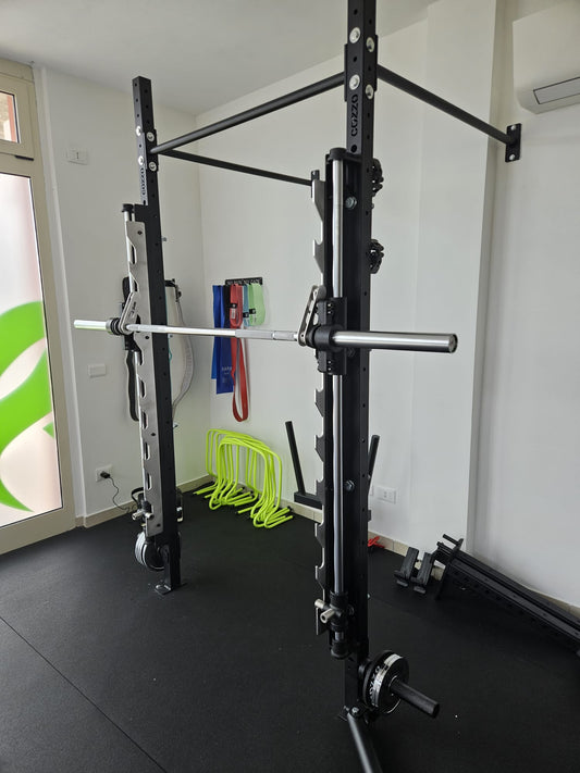 Foto reale del Sistema Smith Machine Cozzo Strength Equipment integrato su una campata Rig professionale, con bilanciere olimpionico da 20kg in posizione.