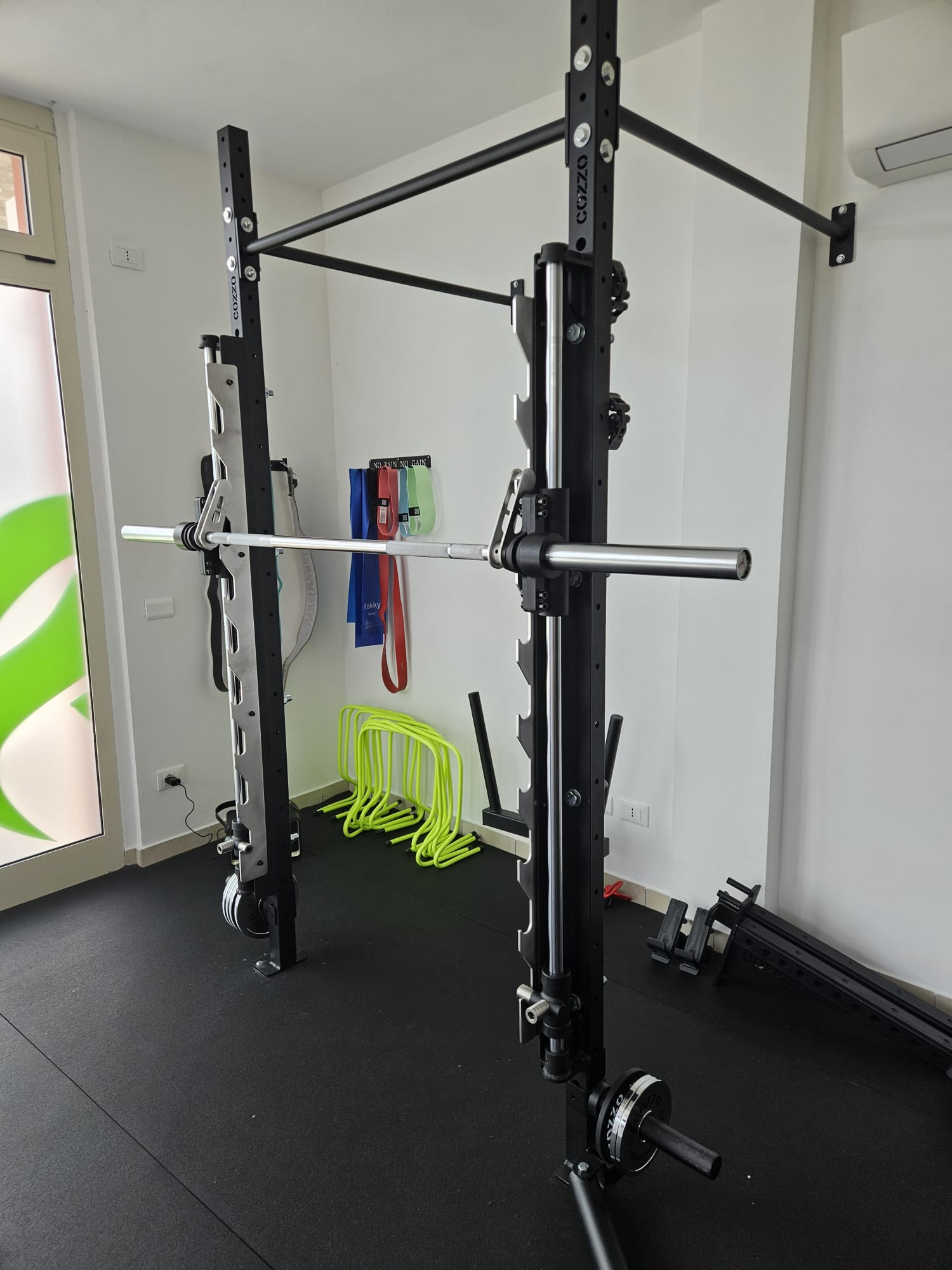 Foto reale del Sistema Smith Machine Cozzo Strength Equipment integrato su una campata Rig professionale, con bilanciere olimpionico da 20kg in posizione.